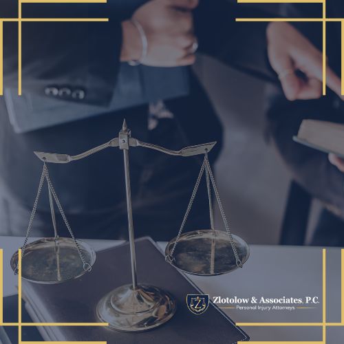 A balance scale sits on a desk with legal documents, while two people in business attire are visible in the background, highlighting Zlotolow & Associates, P.C., your trusted personal injury lawyer in Brooklyn.